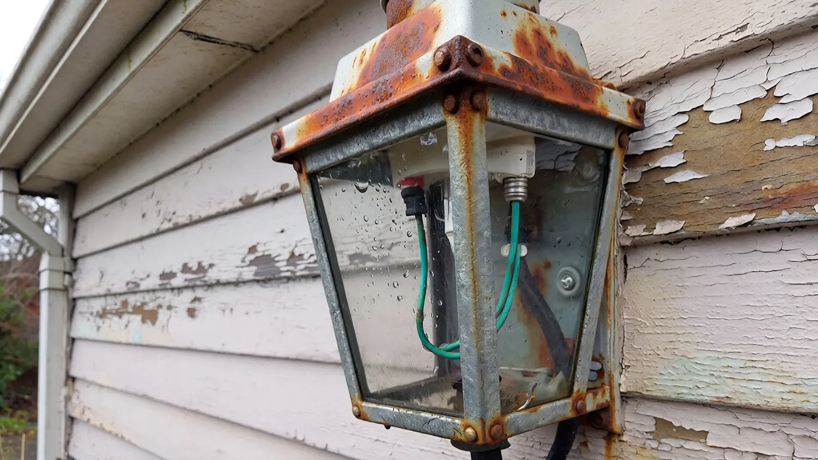 Weathered outdoor light fixture showing rust, internal corrosion, and moisture damage inside the housing.