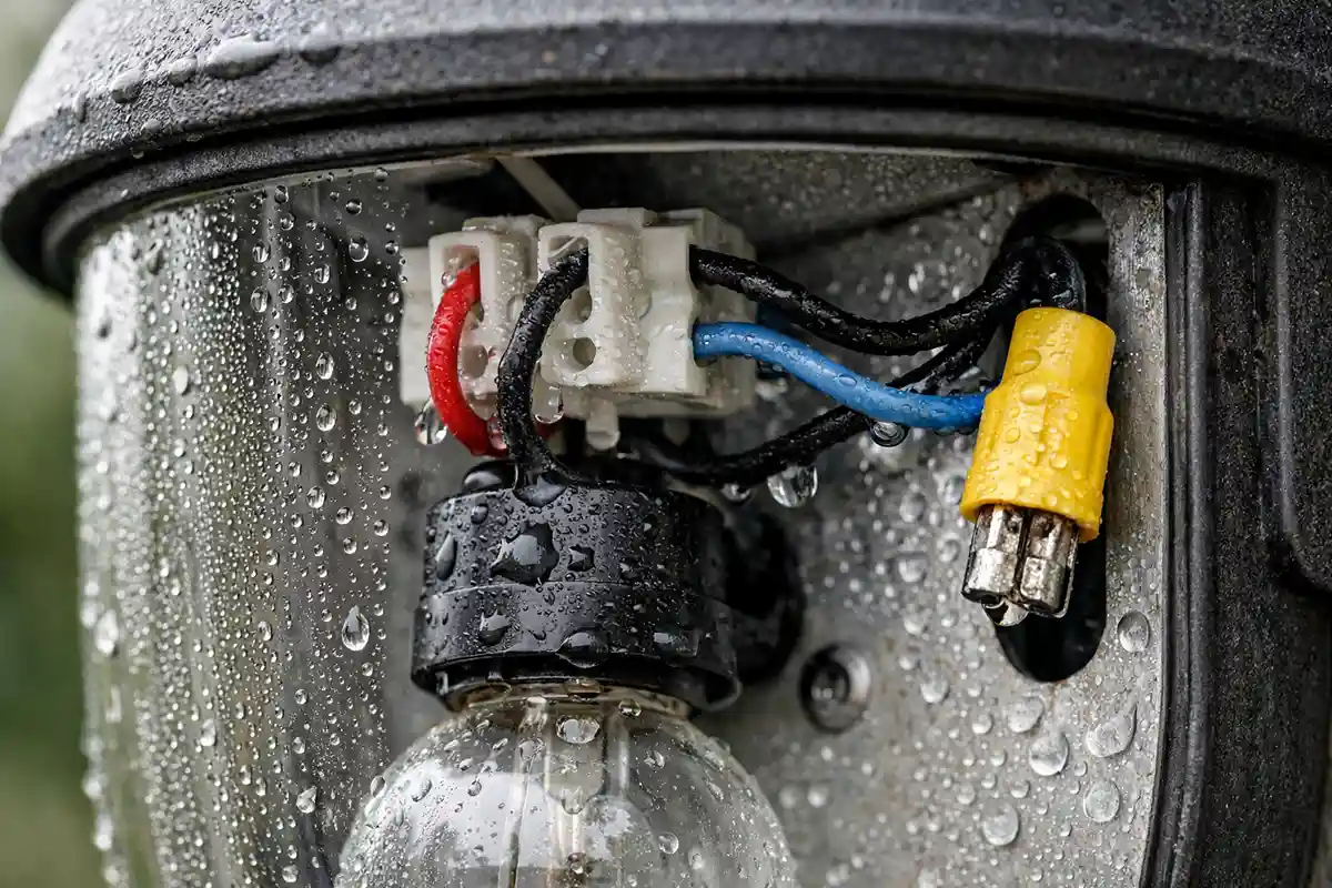 Water droplets and condensation inside an outdoor wall light fixture showing moisture accumulation around electrical connectors.