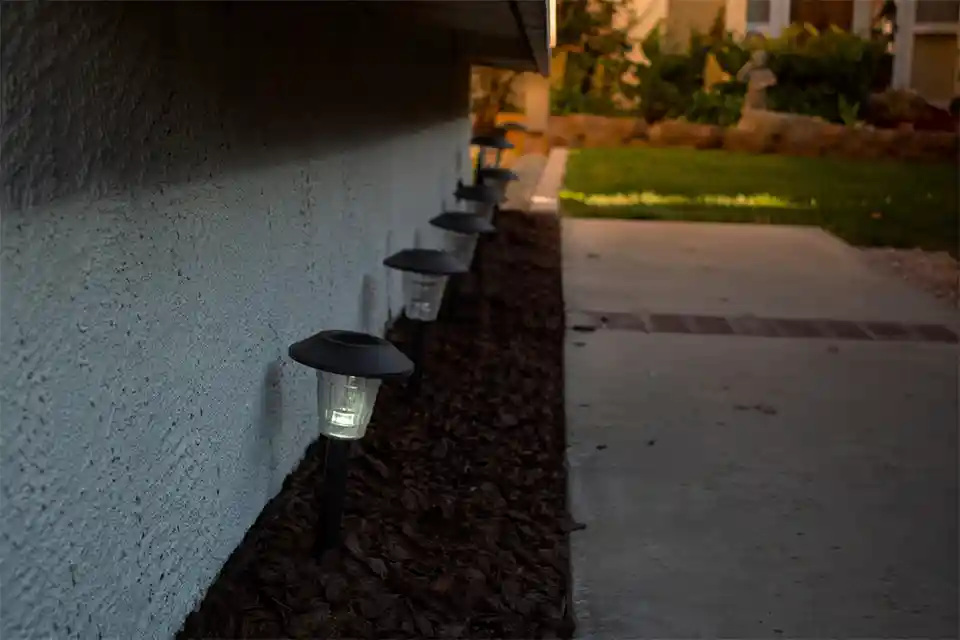 Solar path lights under a roof overhang with shade covering the top panels and dim output at dusk along a front walkway.
