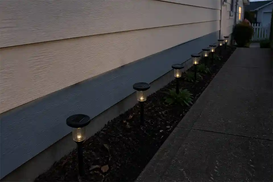 Solar garden lights along a north-facing house wall with heavy shade and weak light output at dusk