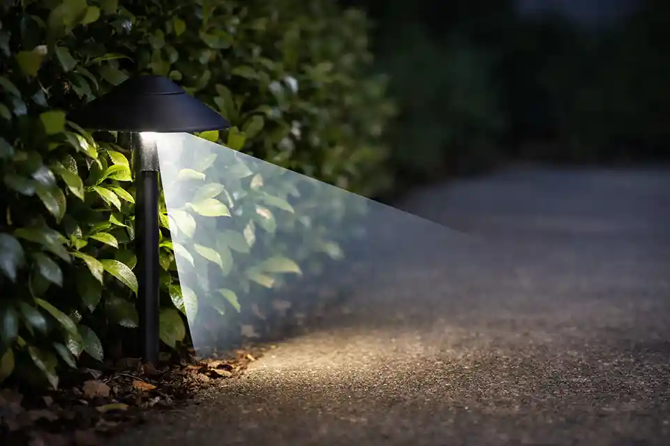 Outdoor path light beside dense shrubs with overlay showing the beam blocked before reaching the walkway