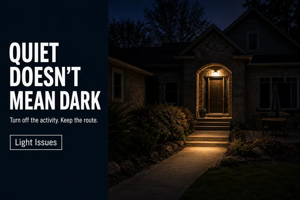 Quiet home exterior with patio lights off and low warm entry lighting preserving the necessary nighttime route.